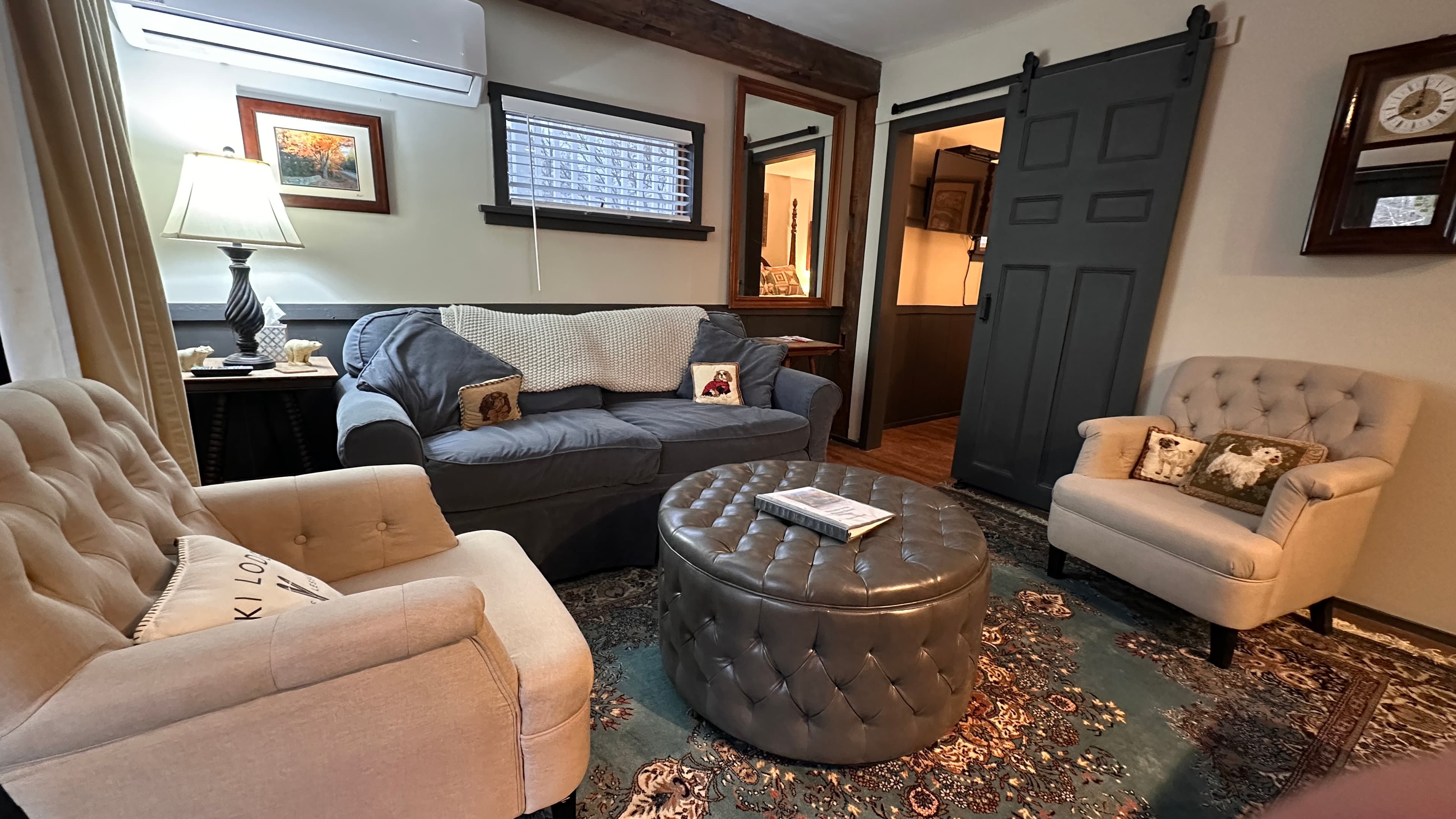 A warm and inviting living area with a gray sofa, two cozy beige armchairs, and a tufted ottoman.