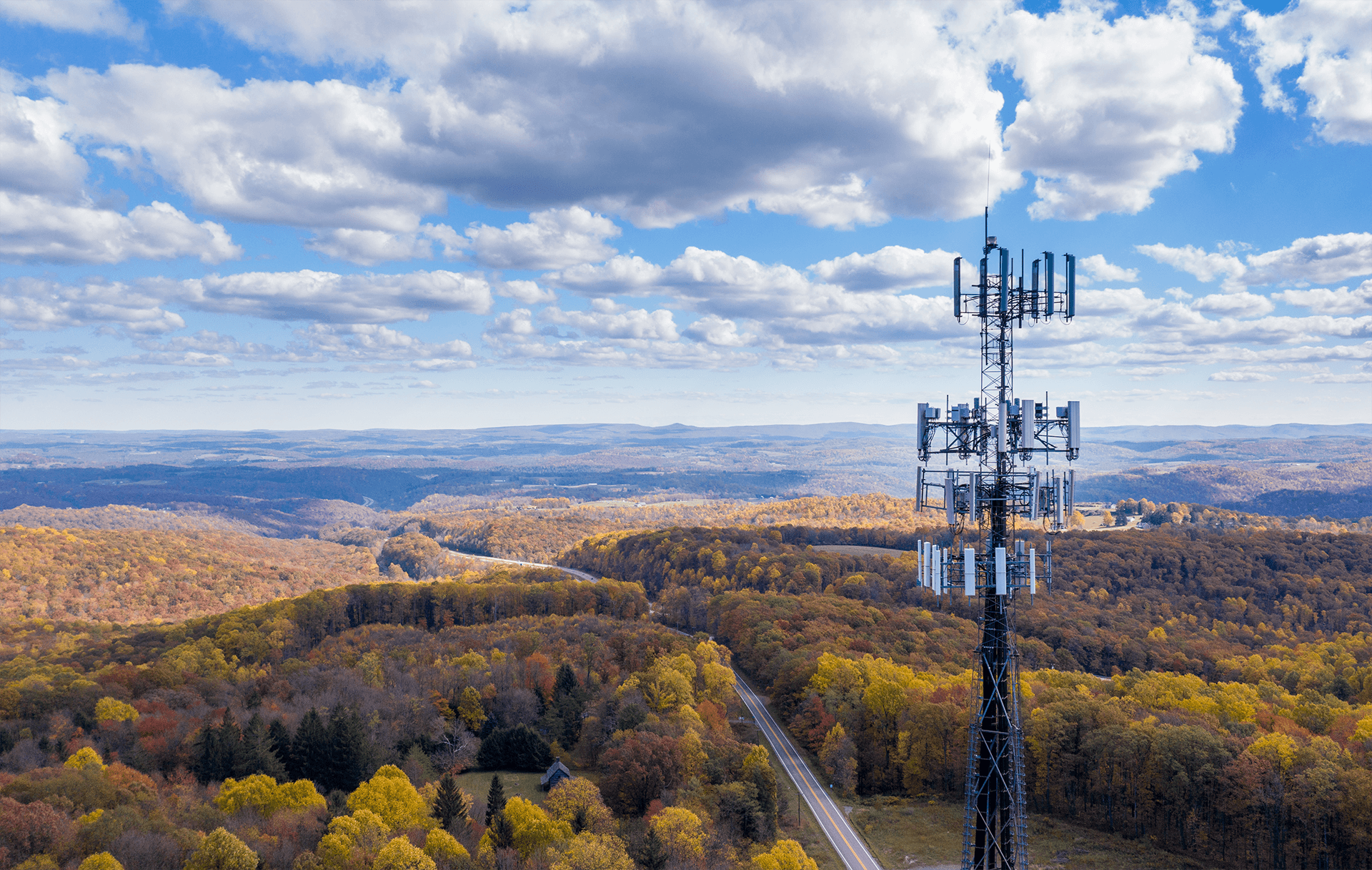 A cell tower stands atop a ridge overlooking a colorful autumn landscape and a winding road below. A cell tower stands atop a ridge overlooking a colorful autumn landscape and a winding road below.