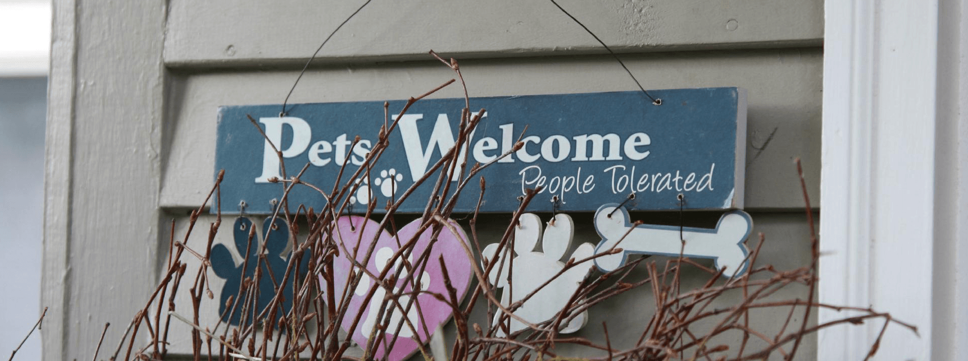 A sign reading "Pets Welcome, People Tolerated," with decorative paw prints and a bone.