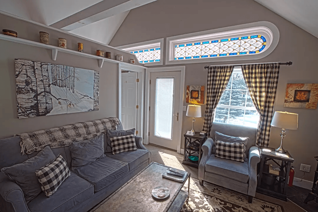 A cozy living room featuring a blue sofa with plaid pillows, two armchairs, a coffee table, and a decorative window with stained glass.
