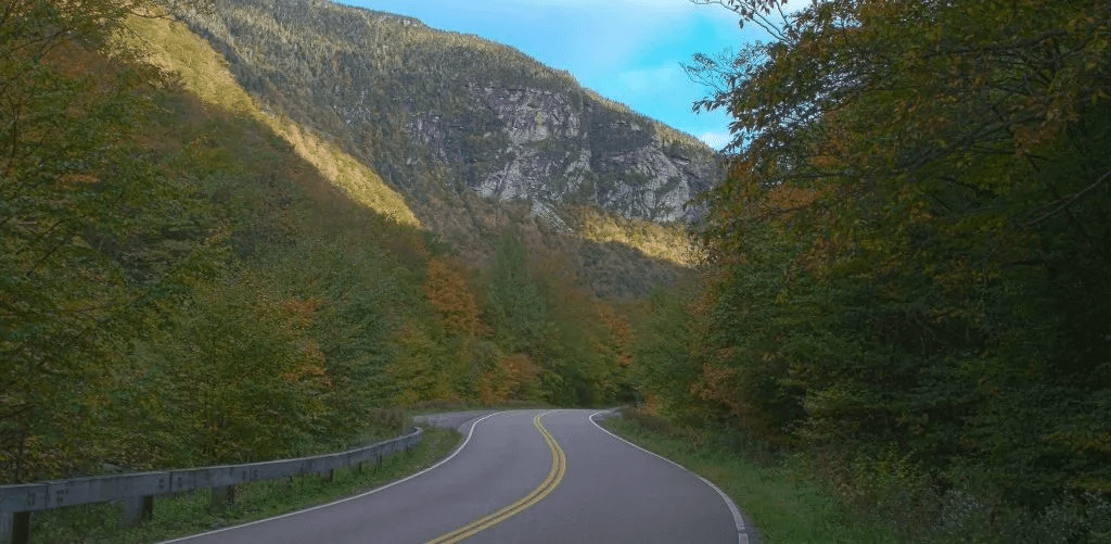 A winding road through colorful autumn trees and mountainous terrain under a clear sky.