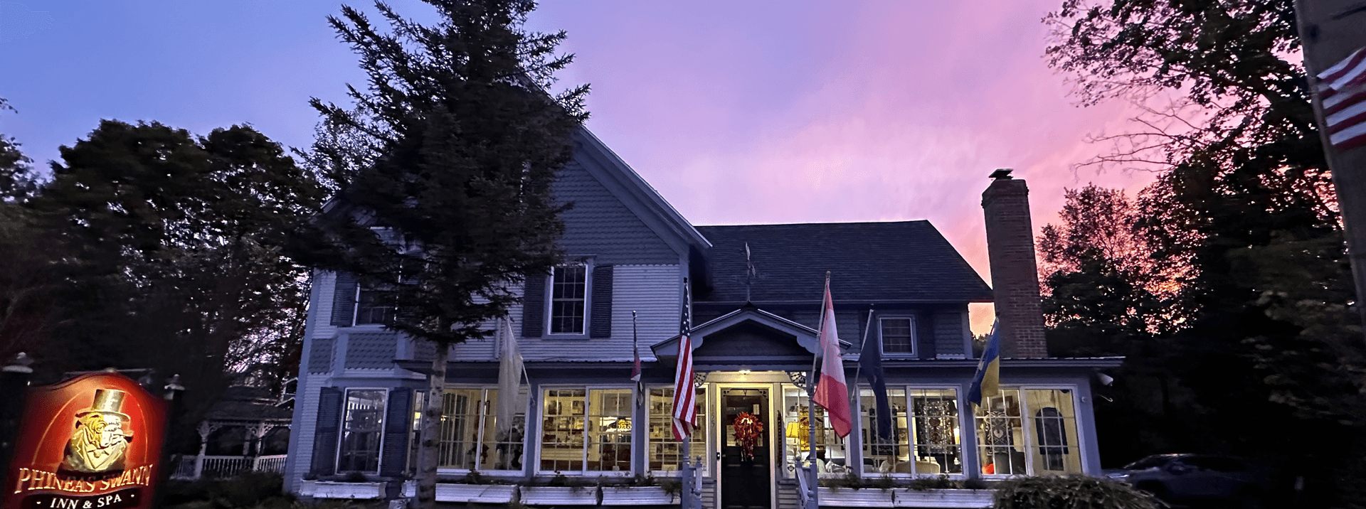 A charming inn with a purple sunset backdrop, featuring multiple flags and lush greenery.