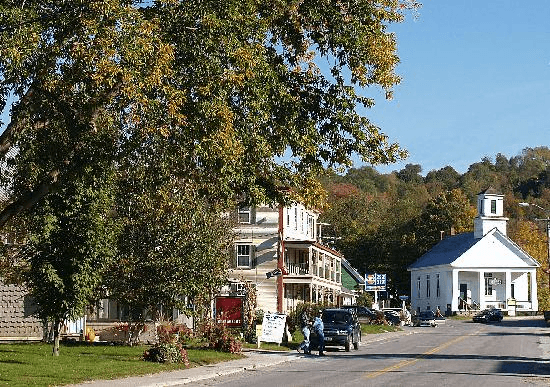 A quaint town street featuring a church, shops, and autumn foliage.