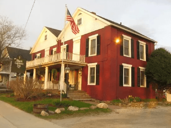 Red and white inn with a large porch and American flag in front. Red and white inn with a large porch and American flag in front.
