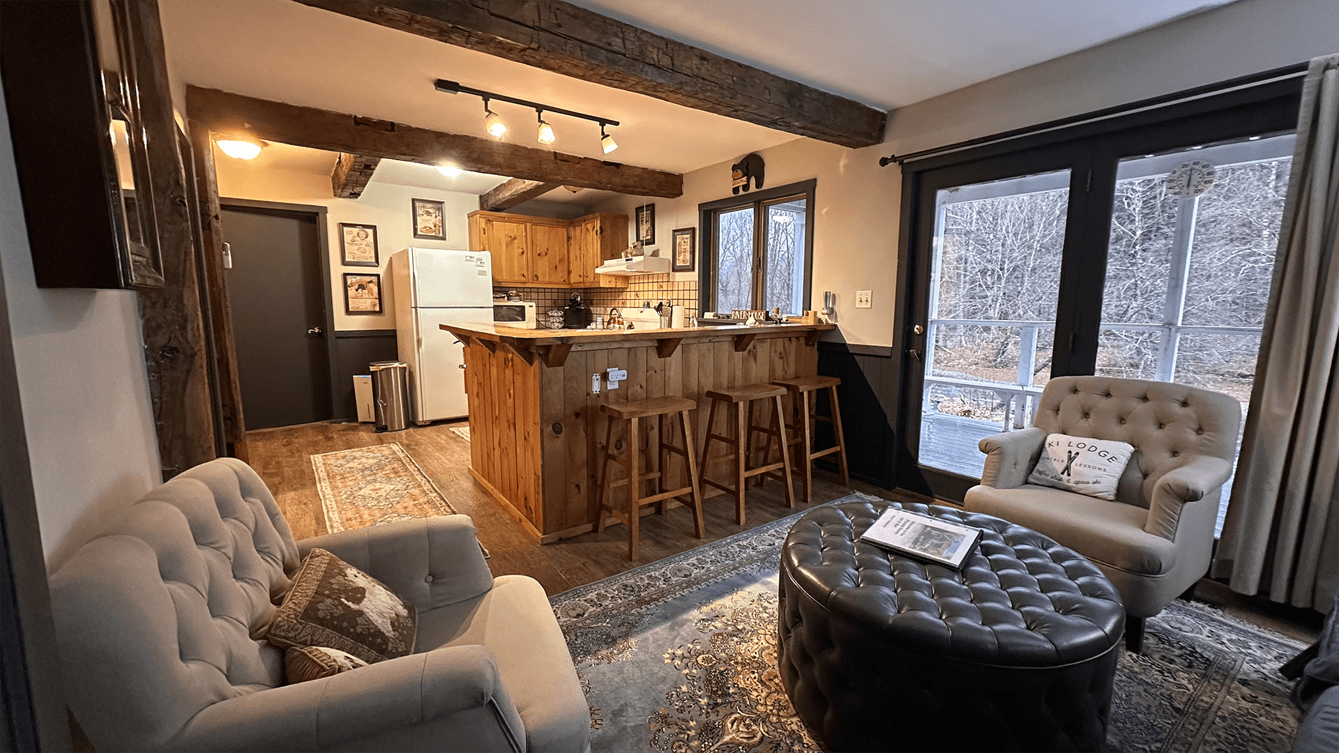 A cozy living area featuring a kitchen bar, two armchairs, a round coffee table, and large windows with outdoor views. A cozy living area featuring a kitchen bar, two armchairs, a round coffee table, and large windows with outdoor views.