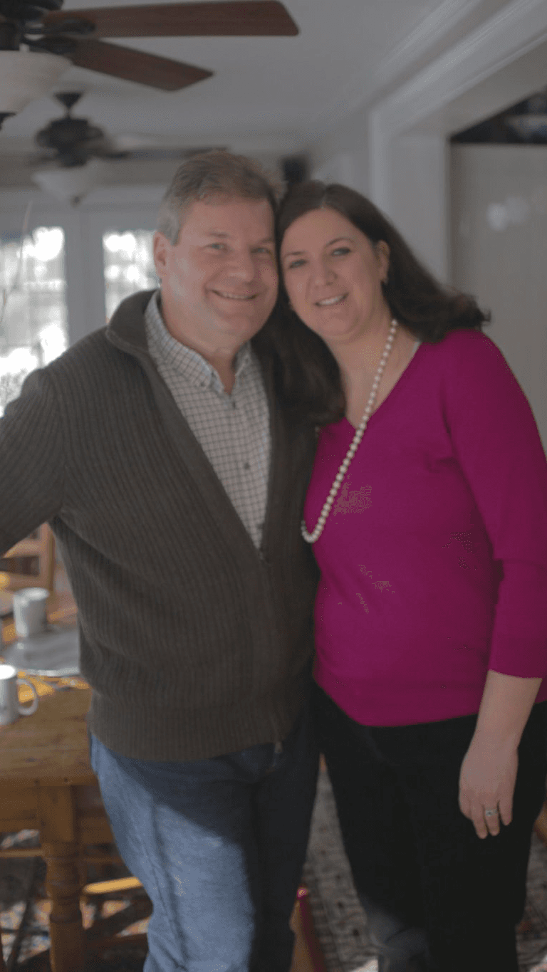 A man and woman smile together in a warmly lit indoor setting.