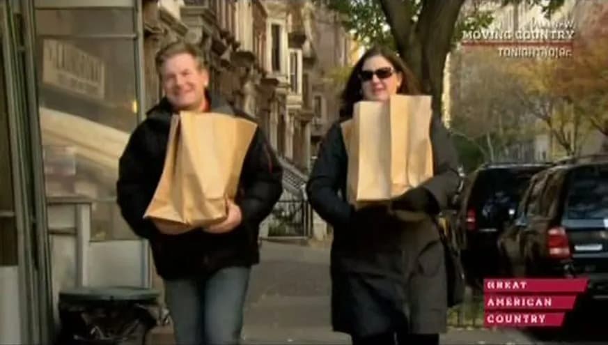 Two people walk down a city street carrying paper bags, smiling. Two people walk down a city street carrying paper bags, smiling.