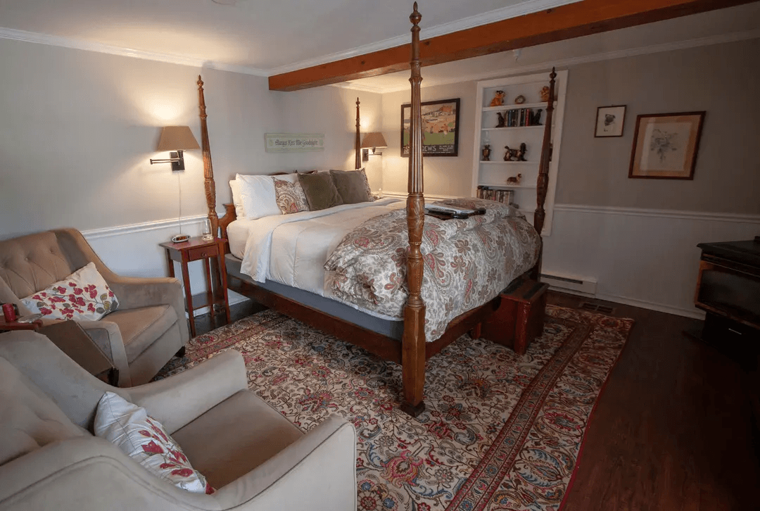 A cozy bedroom featuring a four-poster bed, a plush armchair, and a decorative area rug.