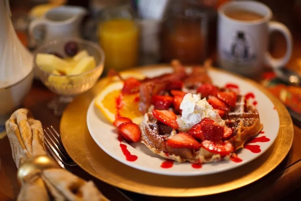 A plate of waffles topped with strawberries, whipped cream, and a drizzle of sauce, accompanied by various breakfast beverages. A plate of waffles topped with strawberries, whipped cream, and a drizzle of sauce, accompanied by various breakfast beverages.